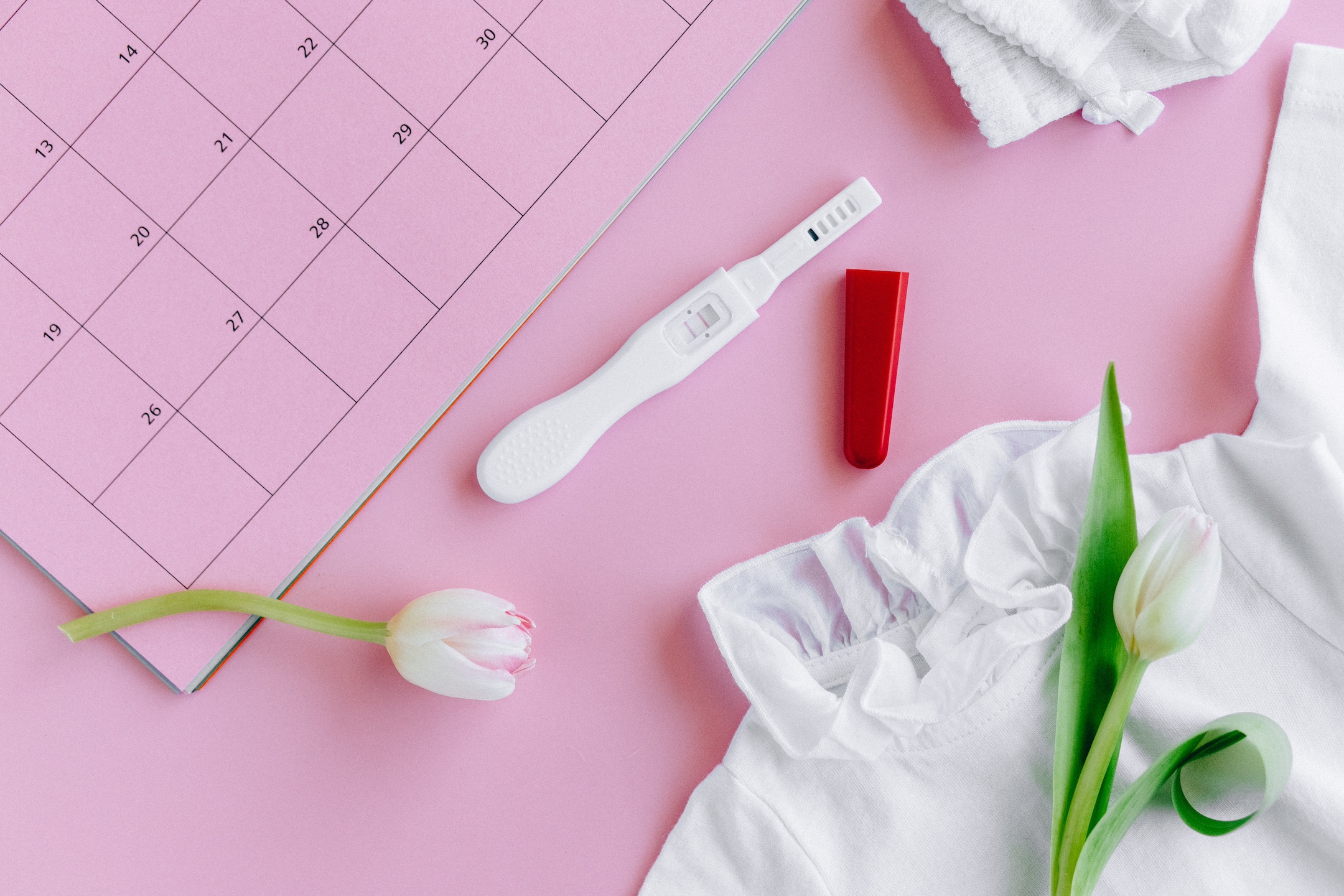 positive pregnancy test sits next to a planning calendar on a pink background, understanding your menstrual cycle, role in pregnancy, pregnancy hormones, fertility coaches near me