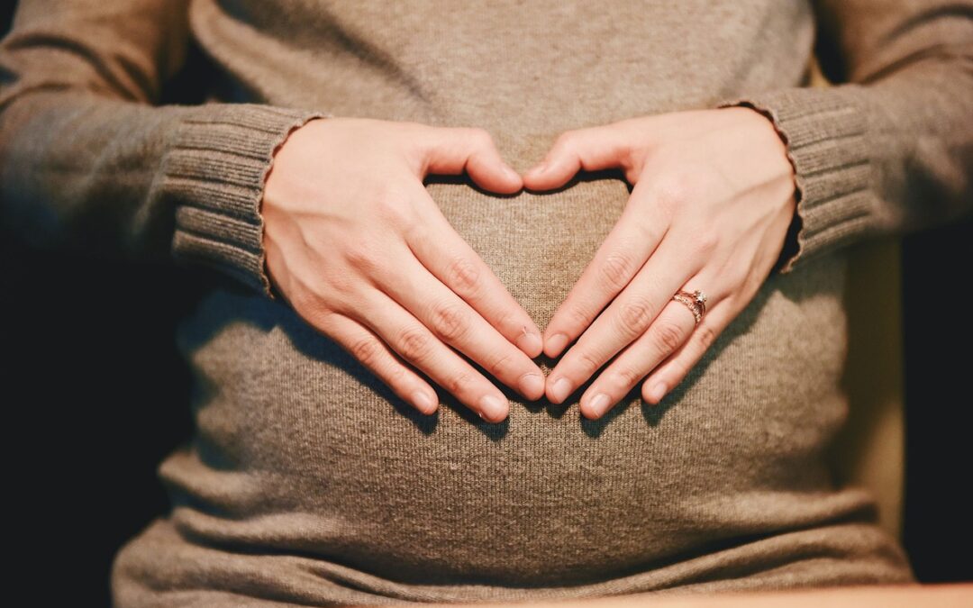 woman holding her hands in a heart shape over her pregnant belly. Influence of Chiropractic Care on Fertility