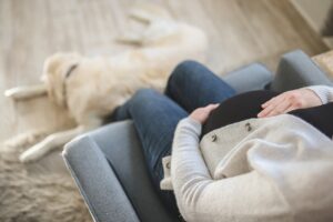 Woman sitting holding her pregnant belly with a dog at her feet.